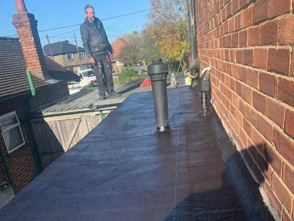 A newly covered flat roof on a single-storey brick extension, with a roofer standing at the far end