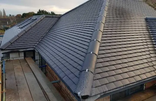 A newly finished roof in grey tiles with a dry ridge and dry verge, seen from the scaffold boards along the eaves