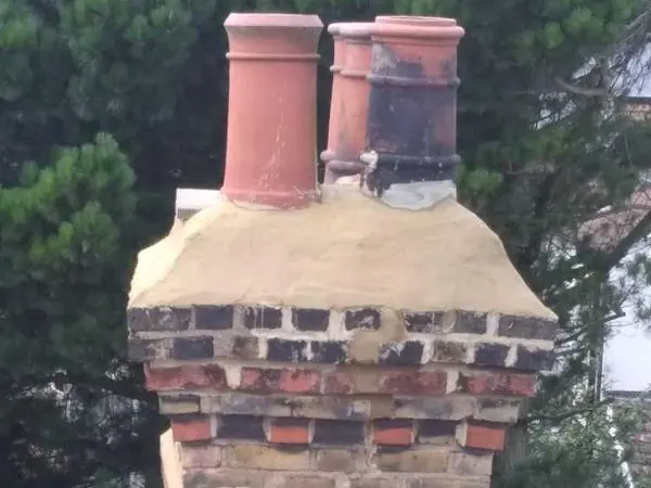A rebuilt brick chimney stack with a new mortar crown and two clay chimney pots, above a tiled roof